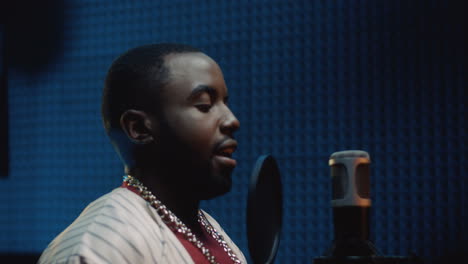 young attractive man singing a song in the microphone at the sound studio, then taking on a cap and smiling t the camera