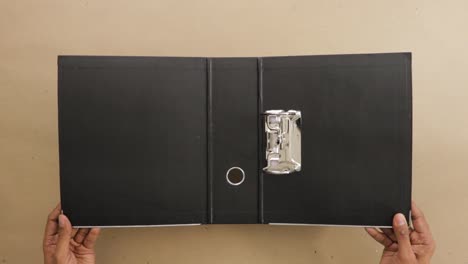 Holding-open-black-lever-arch-file-with-ring-binder-on-office-desk