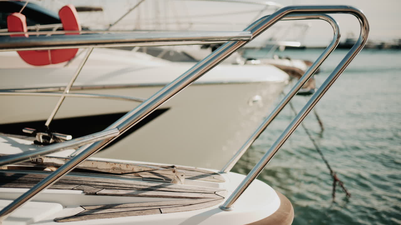 Close up of chrome railing and wooden deck of a luxury yacht docked in a marina under golden light