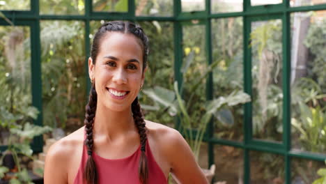 smiling woman with braided hair posing in yoga attire in glass house, copy space