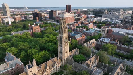 harkness tower at yale old campus university of new haven. american city in connecticut at sunset. summer day with green trees. industrial waterfront in distance. aerial tilt up wide shot