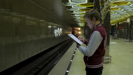 un adolescente usando una tableta en una estación de metro