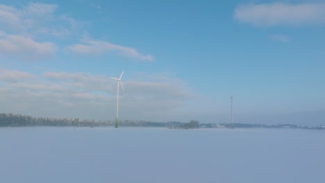 aerial view of wind turbines generating renewable energy in the wind farm, snow filled countryside landscape with fog, sunny winter day, wide drone shot moving forward