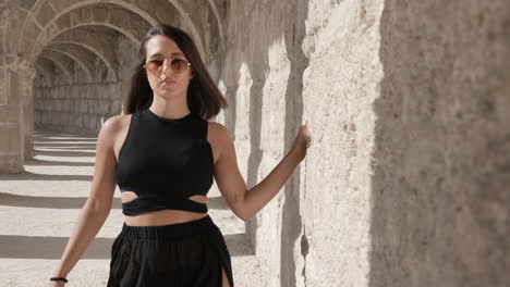 young beautiful woman walking under arches by ancient roman walls, covering camera lens transition