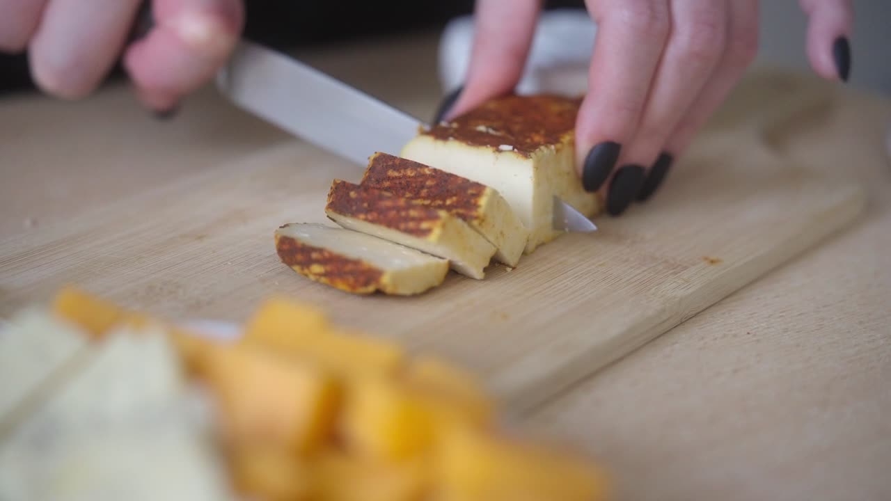 Close-up of a woman's hand slicing a spicy cheese. Food preparation at home.