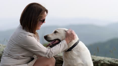 Woman-pets-white-lab-dog-with-mountains-in-background