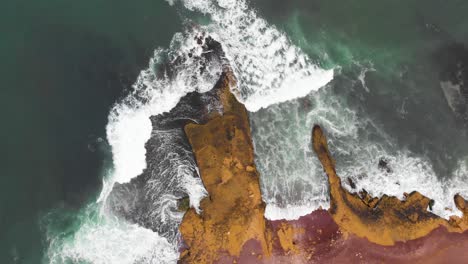 Descending-spinning-aerial-shot-of-waves-crushing-in-to-a-huge-cliff-at-the-ocean-coastline