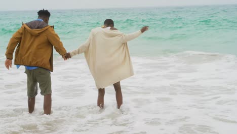 Vista-Trasera-De-Una-Pareja-Afroamericana-Jugando-Con-Olas-Del-Mar-En-La-Playa-4k