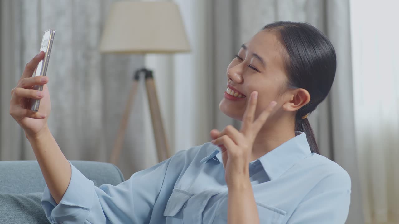 휴대전화를 이용한 즐거운 아시아 여성이 거실의 소파에 누워서 셀카를 찍는 장면