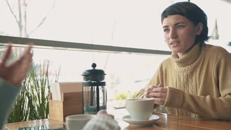 young woman talking to her friend and having a cup of tea and a coffee