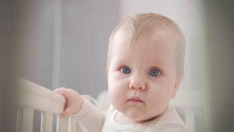 cute baby face with blue eyes. infant baby standing in bed and looking around