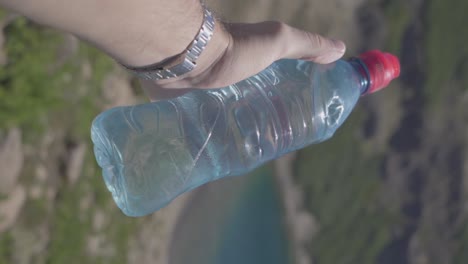 a man holding a water bottle in his hand next to a lake and forest in the moiuntains in summer