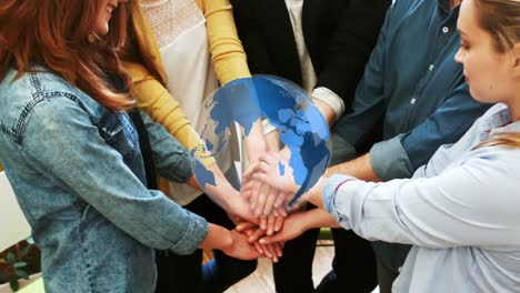 Animation-of-spinning-globe-over-diverse-colleagues-stacking-their-hands-together-at-office