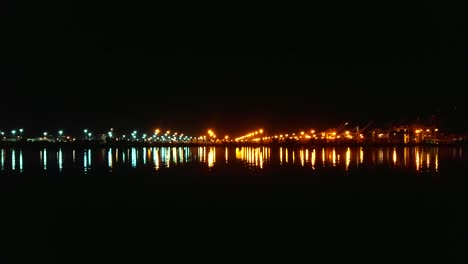 una panorámica lenta a la derecha a través de las aguas resplandecientes con luces de la industria naviera de la bahía