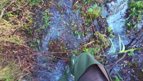 man in tall rubber boots walking in swampy landscape, pov slow motion view