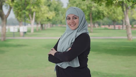 portrait of happy muslim woman standing crossed hands in park