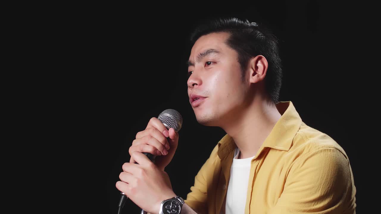 Side View Of Asian Man Singer Holding Microphone And Singing On Black Background
