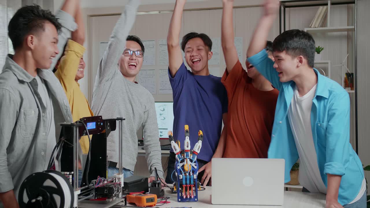 아시안 남자와 노트북과 3d 프린팅을 가진 소년들은 학교에서 사이보그 손에 대해 작업하는 동안 손을 함께 고 골을 외쳤다.