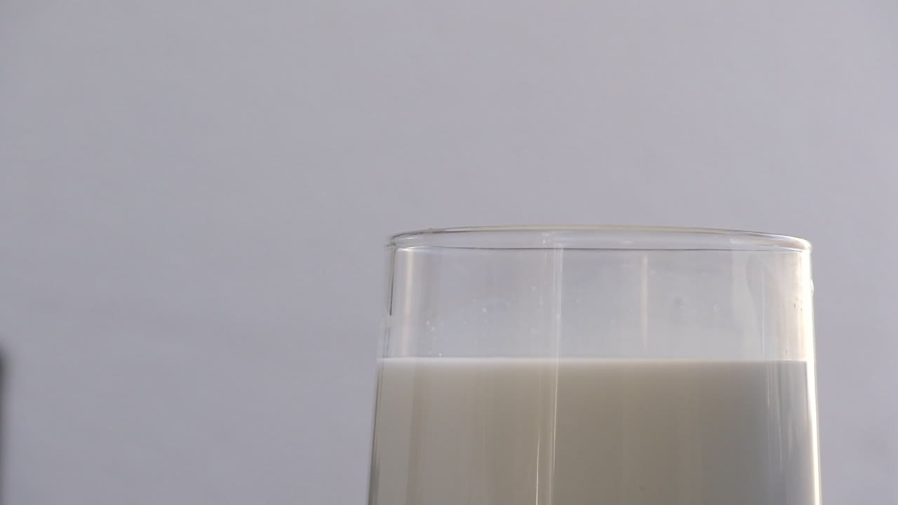 imágenes en cámara lenta de un bloque de hielo que se deja caer en un vaso de leche en un fondo aislado