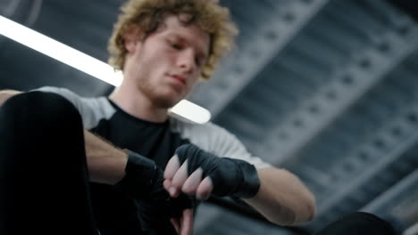 Tired-sportsman-preparing-hands-in-sport-club.-Fighter-using-boxing-tape-at-gym