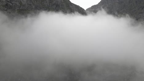 Tall-mountain-range-standing-above-fluffy-cloudscape,-aerial-drone-shot