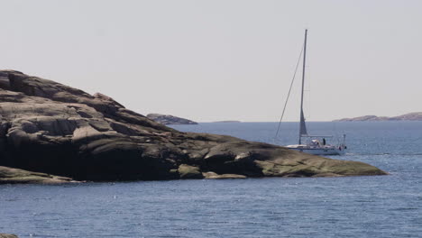 sailboat vanishing behind coastal rocky shore, serenity at sea concept, wide shot