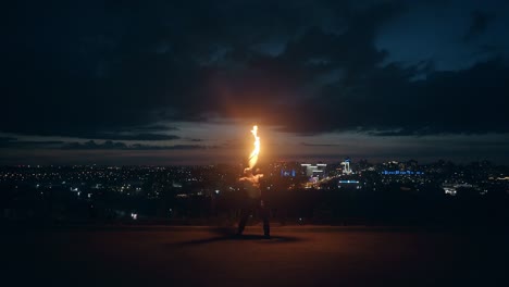 young blond male does tricks with fire breaths fireball in the middle of the night with city skyline 2