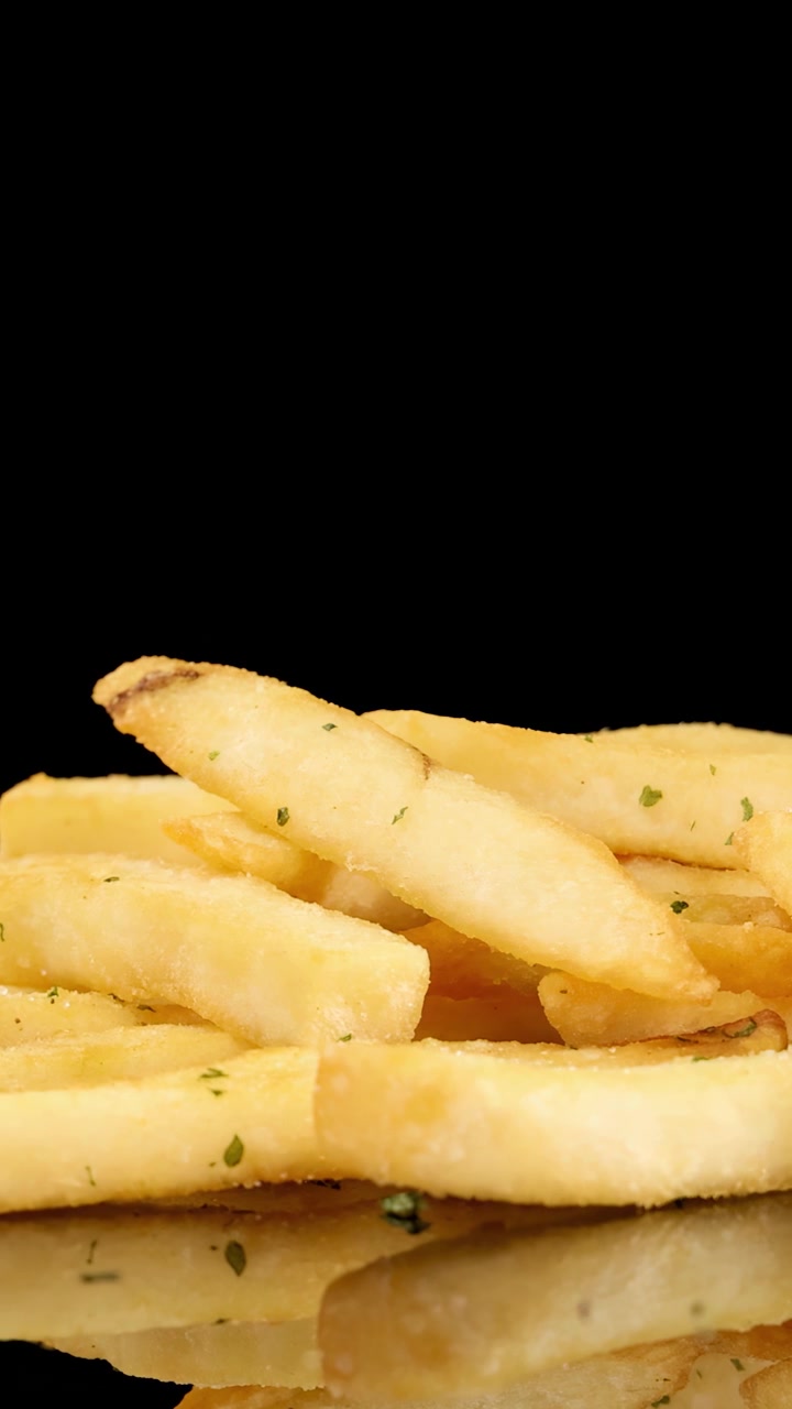Golden French fries rotate smoothly on a reflective surface with dramatic studio lighting and a seamless black background, highlighting texture and crispness in high resolution