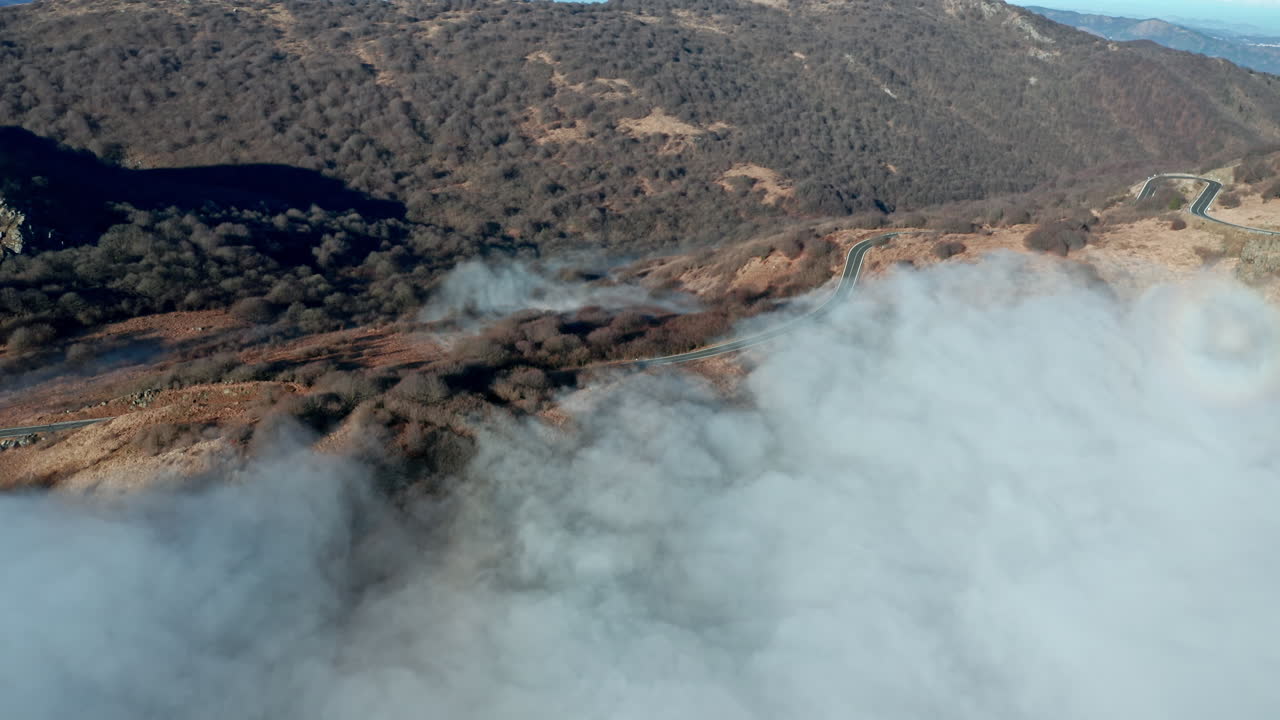 caminos sinuosos a través de colinas con nubes bajas, luz matutina, vista aérea