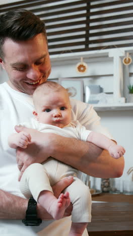 happy caucasian dad holding his newborn son. smiling man wearing white t-shirt kissing a baby in his hands on the head. vertical video
