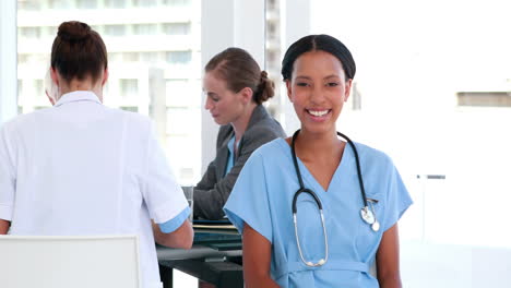 Happy-doctor-looking-at-camera-with-her-colleagues-behind-