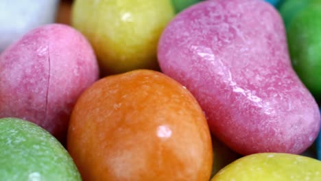 pile of many round chewy candies dragee in multicolored glaze rotate slowly on turntable.