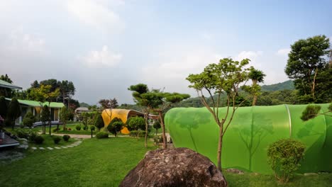 a timelapse of clouds moving over the colorful and unique leaf-shaped buildings of the luxury glam tree glamping resort, set in a beautiful garden in the mountains of south korea