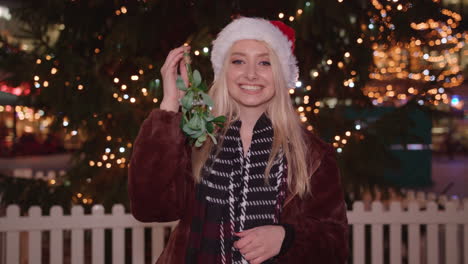 beautiful woman blows you a kiss whilst holding mistletoe