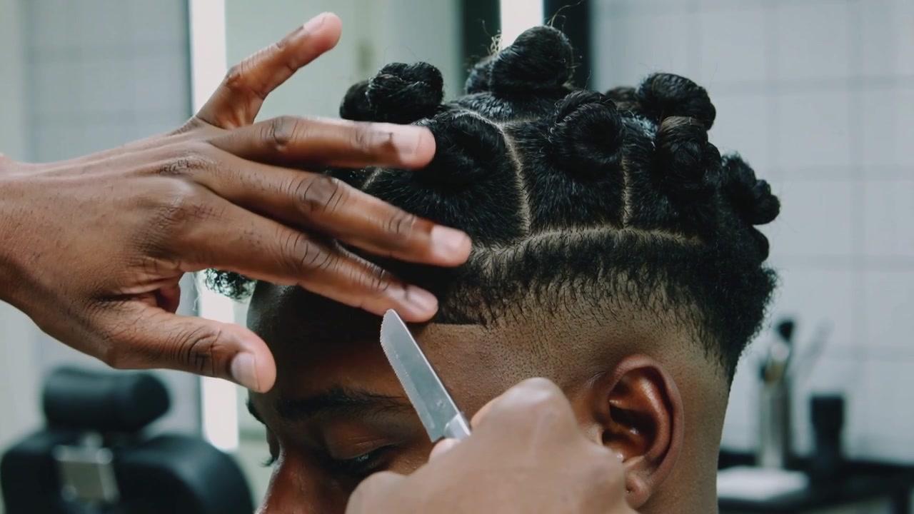 Sollevando i capelli, il barbiere guida un rasoio a mano libera in una barberia, definendo l'attaccatura dei capelli e mantenendo chignon attorcigliati.