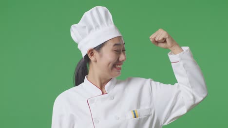 close up de la mujer asiática chef sonriendo y flexionando su bíceps mientras está de pie en el estudio de fondo de la pantalla verde