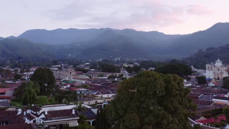 Tiro-De-Drone-Revela-San-Francisco-La-Gran-Basílica-En-Antigua,-Guatemala,-Al-Amanecer,-Con-Nubes-Rosadas-Y-Montañas-Azules-En-El-Fondo