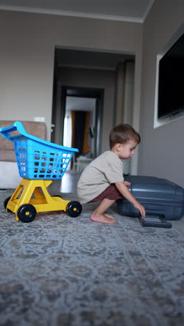 four-year-old toddler pushes a big suitcase and puts it on the floor. a shopping cart stands beside. vertical video.