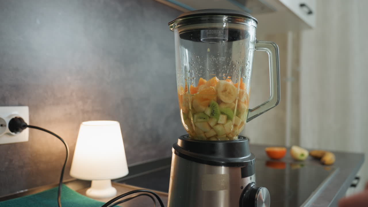 Gravid kvinne starter blender, hender trykker på bryteren for å aktivere apparatet, sitrus og avokado synlig i beholderen, varmt lampelys, rolig kjøkkenbenk, bevisst blanding av prenatal snacks