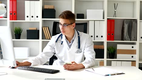 joven médico con el teléfono en la mano y trabajando detrás de la computadora