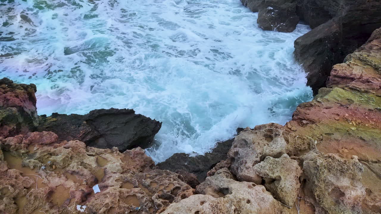 escena costera rocosa donde las olas blancas turbulentas chocan contra rocas dentadas de color marrón rojizo