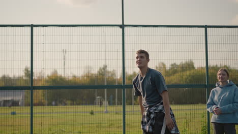 man during volleyball training session throws ball to someone in background, catches it back with lady in cyan hoodie watching and another lady observing, teamwork and training atmosphere