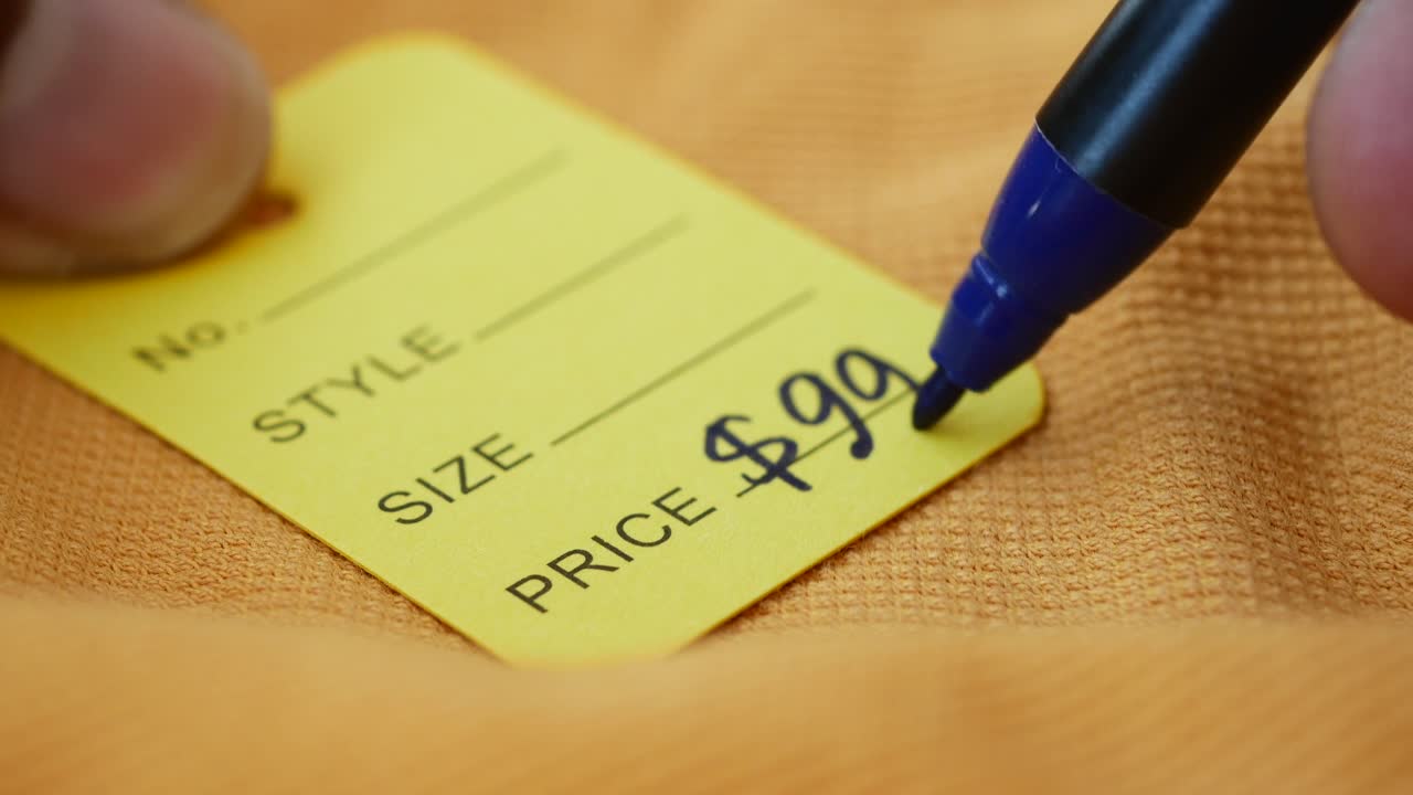 A hand writing the price on a yellow tag with a blue marker