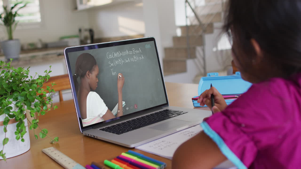 chica afroamericana haciendo la tarea mientras tiene una videollamada con una maestra en una computadora portátil en casa