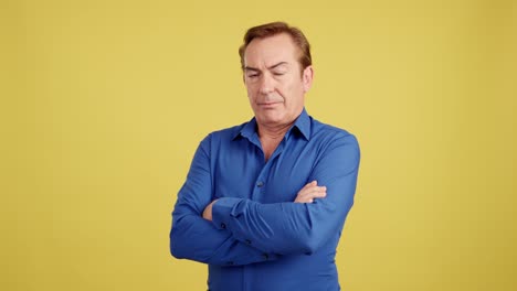 middle-aged man in blue shirt with arms crossed on yellow background