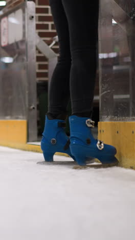primer plano de alguien patinando en patines azules con pantalones negros en una pista de hielo, con otras personas patinando