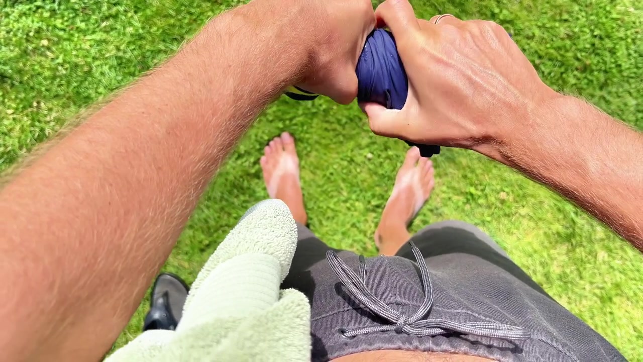 Una persona strizza l'acqua in eccesso da un costume da bagno blu stando a piedi nudi sull'erba verde. Ideale per attività estive, ricreazione all'aperto, costumi da bagno e contenuti sull'igiene