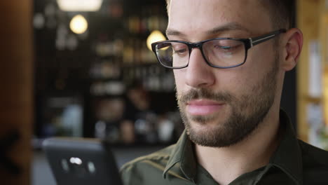 man in glasses uses smartphone in cafe