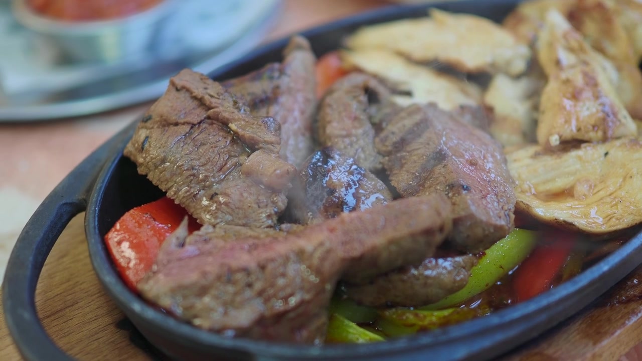 Plato caliente humeante con carne de res, pollo y verduras a la parrilla
