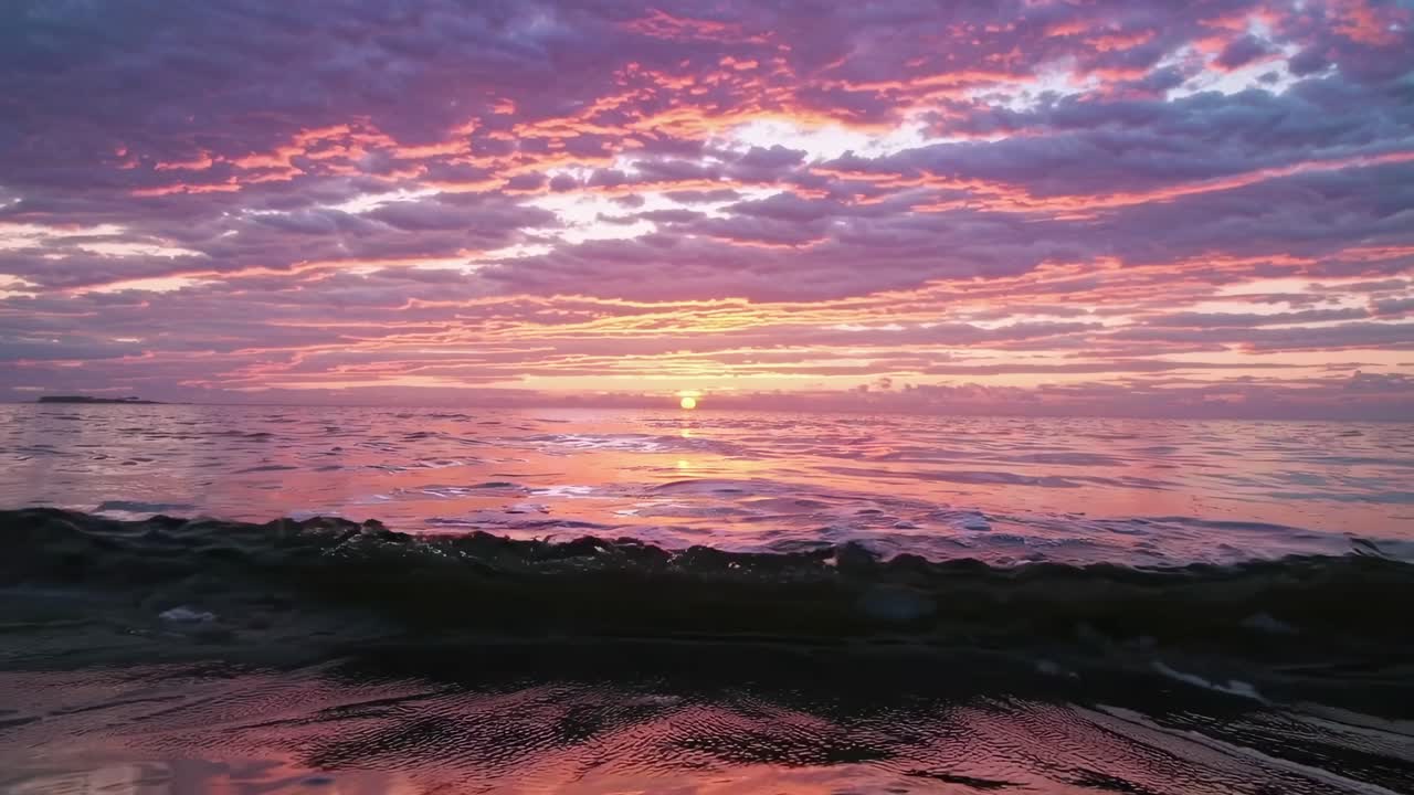 Low-angle video capture of a vibrant sunset over the ocean, with dramatic clouds and reflections